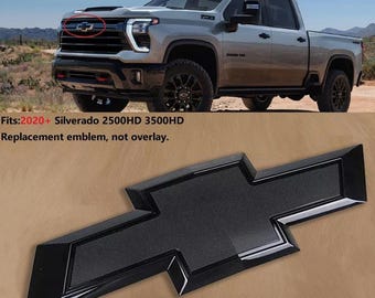 May include: A black replacement emblem for a Chevrolet Silverado truck. The emblem is a bow tie shape with a textured center and glossy black border. The image also shows the truck and text that reads "Fits: 2020+ Silverado 2500HD 3500HD Replacement emblem, not overlay."