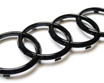 May include: Black emblem featuring four interlocking rings, a recognizable automotive logo. The rings are glossy and appear to be made of a durable material. The emblem is designed for vehicle applications.