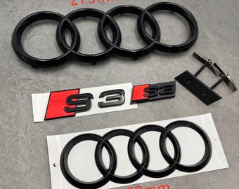 May include: Black car emblem set including the Audi rings (273mm and 192mm), S3 logo with red accents, and a small black component. The emblems are on a gray surface.