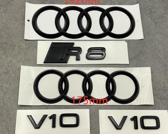 May include: Black car emblems, including the Audi rings measuring 192mm and 175mm, an R8 emblem, and two V10 emblems. The emblems are on white backing paper, ready for application. The image is taken from a top-down perspective.
