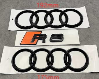 May include: Black car emblems, including the Audi rings in 192mm and 175mm sizes, and an R8 emblem with an orange background. The emblems are on white backing paper.