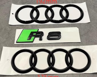 May include: Three black Audi emblem stickers, one measuring 192mm and another 175mm, and a green and black R8 emblem sticker. The Audi emblems feature the iconic four interlocking rings.