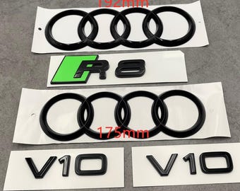 May include: Black car emblems, including two sets of four interlocking rings, a green and black "R8" emblem, and two "V10" emblems. The larger rings measure 192mm, and the smaller rings measure 175mm.