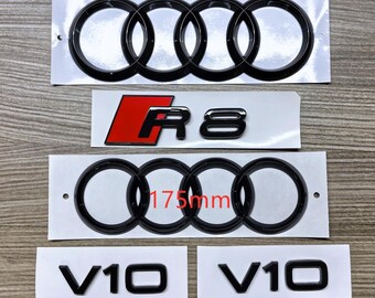 May include: Black car emblems, including two Audi rings measuring 192mm and 175mm, an R8 emblem with red accents, and two V10 emblems. The emblems are on white backing.