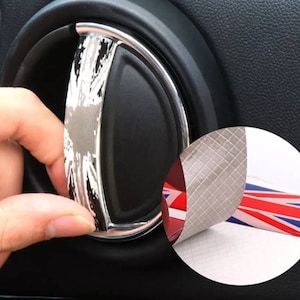 May include: A close-up of a car door handle with a Union Jack design. The handle is black with a chrome ring around it. The Union Jack design is printed on a white background. The handle is being peeled off of a backing sheet.