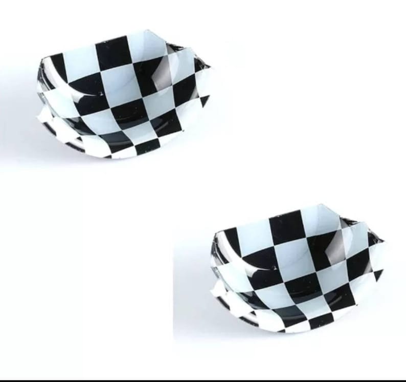 May include: Two black and white chequered car emblems. The emblems are made of plastic and have a slightly curved shape.