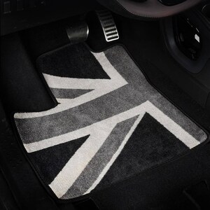 Op de afbeelding: Een zwarte autovloermat met een wit en grijs Union Jack-ontwerp.