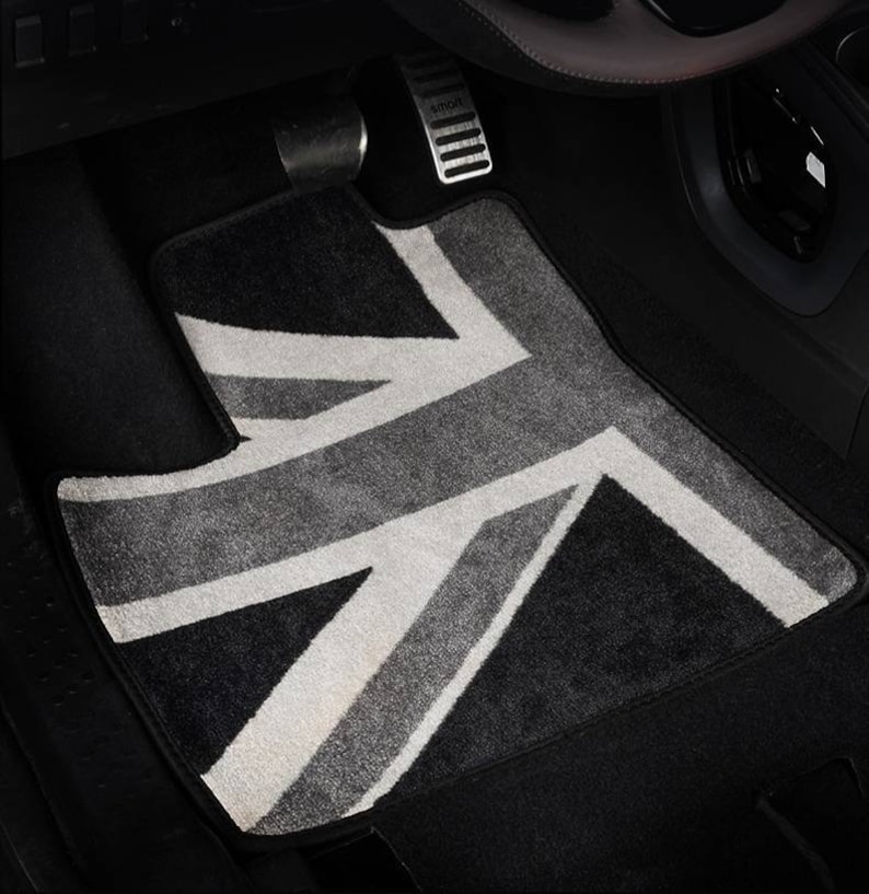 Op de afbeelding: Een zwarte autovloermat met een wit en grijs Union Jack-ontwerp.