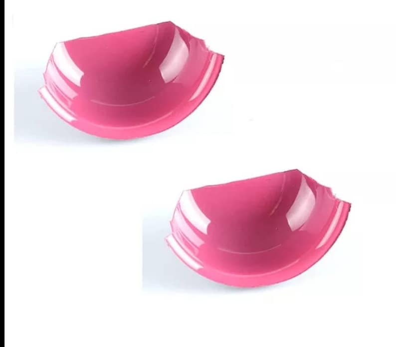 May include: Two pink plastic bra cups, each with a slightly different shape and size.