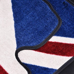 Op de afbeelding: Close-up van een blauw, rood en wit gestreept tapijt met een zwarte rand. Het tapijt is gemaakt van een zacht, pluche materiaal.