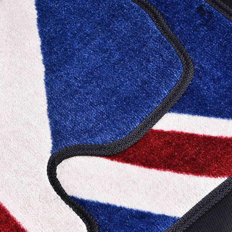 Op de afbeelding: Close-up van een blauw, rood en wit gestreept tapijt met een zwarte rand. Het tapijt is gemaakt van een zacht, pluche materiaal.