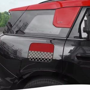 Op de afbeelding: Zwarte auto met rode accenten op het dak en zijpaneel. De tankklep heeft een rode bovenkant en een dambordpatroon. Het woord "ALL4" is zichtbaar op het zijpaneel.