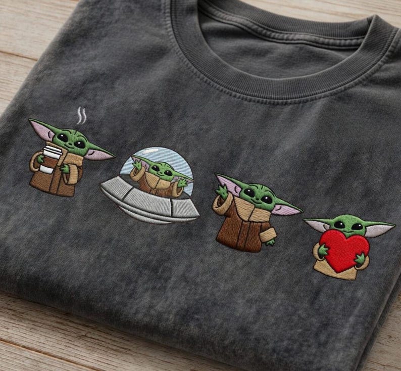 May include: Dark gray t-shirt featuring embroidered images of a green alien character. The alien is depicted holding a coffee cup, in a spaceship, waving, and holding a red heart. The shirt has a crew neck.