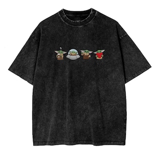 May include: Black acid wash t-shirt featuring a series of four Grogu (Baby Yoda) illustrations. The illustrations depict Grogu with a cup, in a pod, holding a cup, and holding a red heart. The t-shirt has a crew neck and short sleeves.