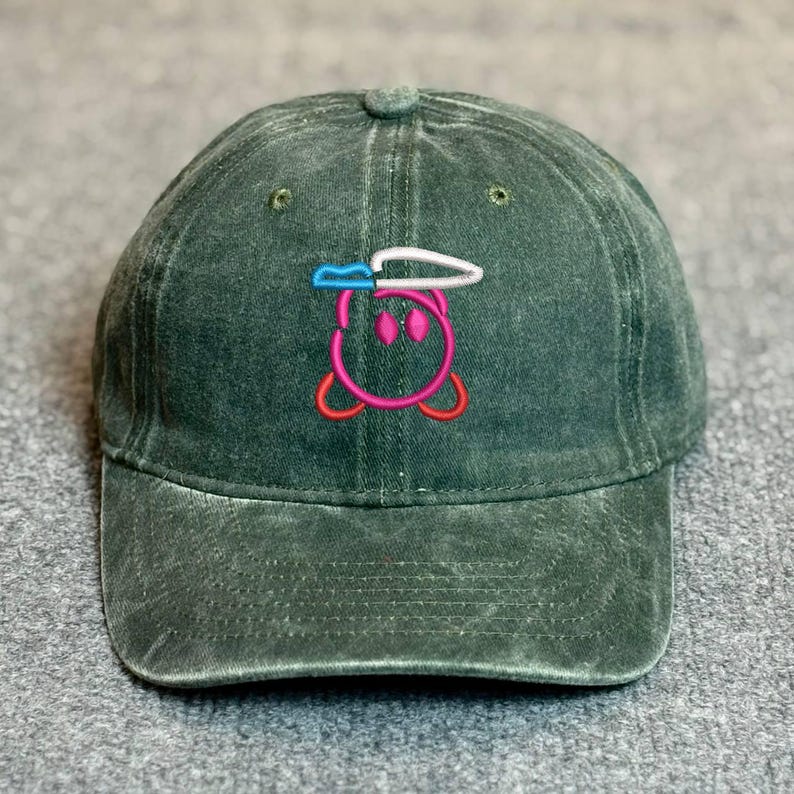May include: Dark green baseball cap with an embroidered cartoon character design. The character is pink with a white and blue hat and a white knife. The cap has a curved brim and a button on top.