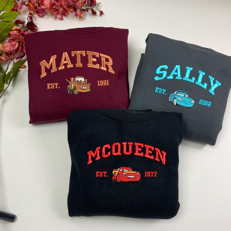 Puede incluir: Tres sudaderas con dise&ntilde;os bordados. Una es granate con "MATER" y un cami&oacute;n de dibujos animados. Otra es gris oscuro con "SALLY" y un coche de dibujos animados. La tercera es negra con "MCQUEEN" y un coche de dibujos animados.