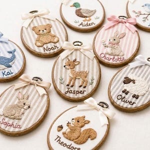 May include: A collection of oval wooden embroidery hoops featuring stitched animal designs on striped fabric. Each hoop displays a unique creature including a whale, bear, duck, bird, rabbit, deer, sheep, and squirrel, with names embroidered below.