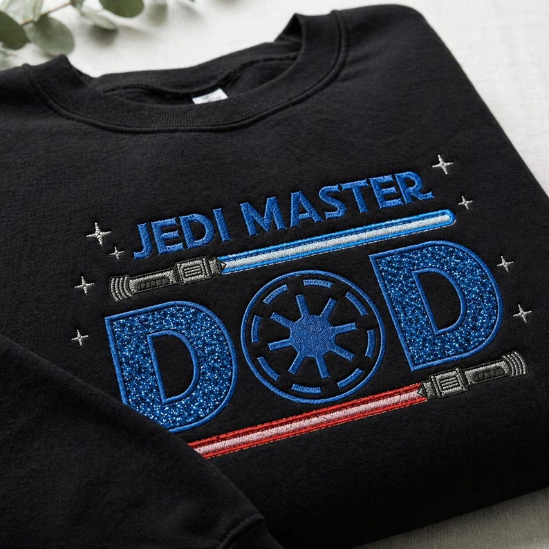 May include: Black sweatshirt with blue embroidered text that reads "JEDI MASTER DAD". The design includes a blue lightsaber, a red lightsaber, and a blue symbol. The letters "D" are filled with a glittery blue material.