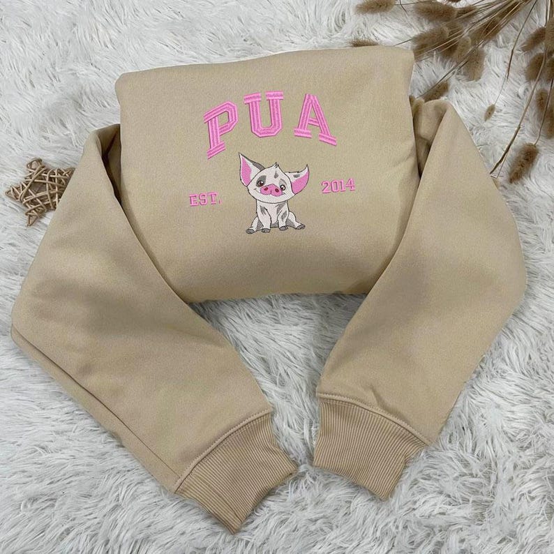 K&ouml;nnte beinhalten: Beigefarbener Pullover mit langen &Auml;rmeln und einem rosa gestickten Schwein mit dem Text "PUA EST. 2014" auf der Vorderseite.