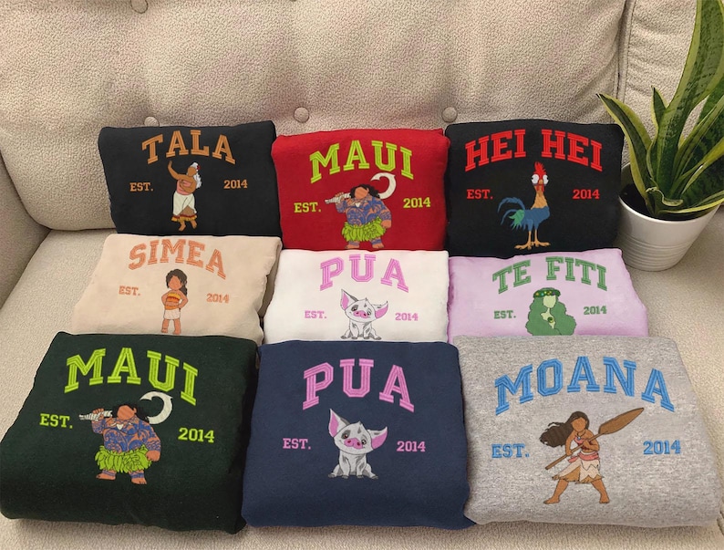 K&ouml;nnte beinhalten: Zehn bunte Sweatshirts mit verschiedenen Designs und Texten. Die Sweatshirts zeigen Figuren aus dem Disney-Film Moana, darunter Maui, Pua und Moana. Der Text auf den Sweatshirts enth&auml;lt die Namen der Figuren, das Wort "EST." und das Jahr 2014.