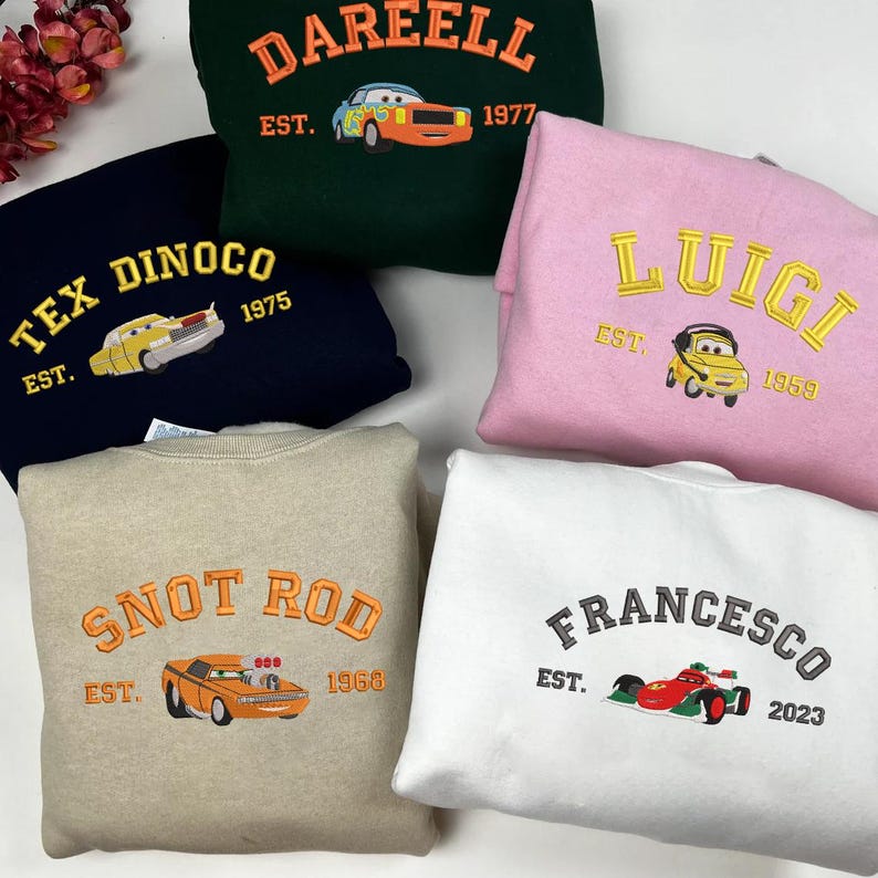 Puede incluir: Una colecci&oacute;n de sudaderas en varios colores, cada una bordada con el nombre de un personaje de coche, un a&ntilde;o y la palabra "EST.". Las sudaderas presentan dise&ntilde;os como "DAREELL", "TEX DINOCO", "SNOT ROD", "LUIGI" y "FRANCESCO".