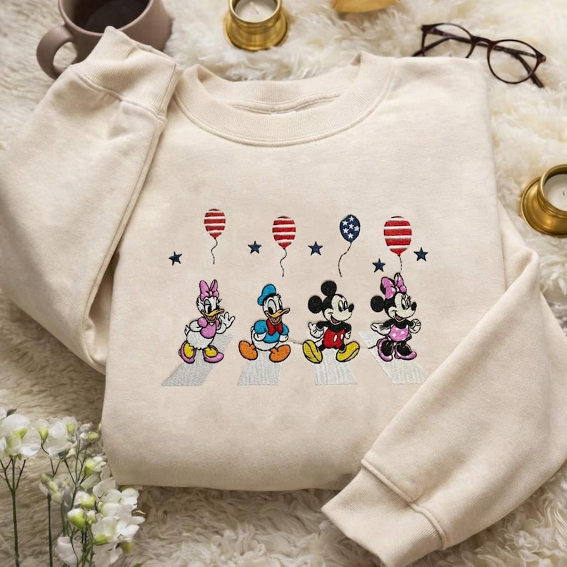 Puede incluir: Sudadera de color crema con un dise&ntilde;o bordado de personajes de dibujos animados caminando con globos. Los globos tienen rayas y estrellas rojas y azules. Los personajes incluyen un pato, un rat&oacute;n y una ratona.
