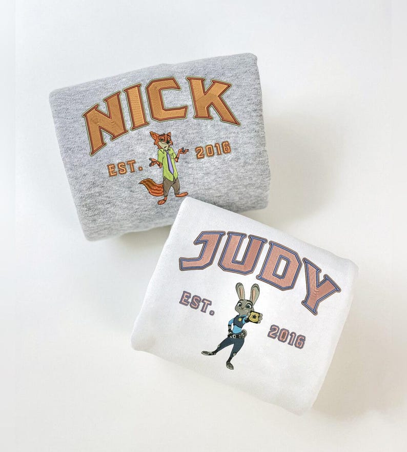 May include: Two folded sweatshirts, one gray and one white. The gray sweatshirt has the name "NICK" in orange lettering with a fox graphic and "EST. 2016". The white sweatshirt has "JUDY" in orange lettering with a bunny graphic and "EST. 2016".