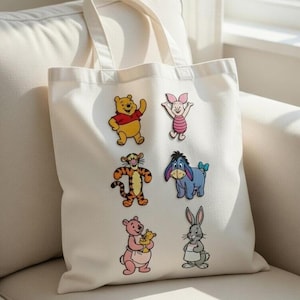 May include: Off-white tote bag adorned with cartoon character patches. The patches depict Winnie the Pooh, Piglet, Tigger, Eeyore, Kanga with Roo, and Rabbit. The bag has a basic design with two handles.