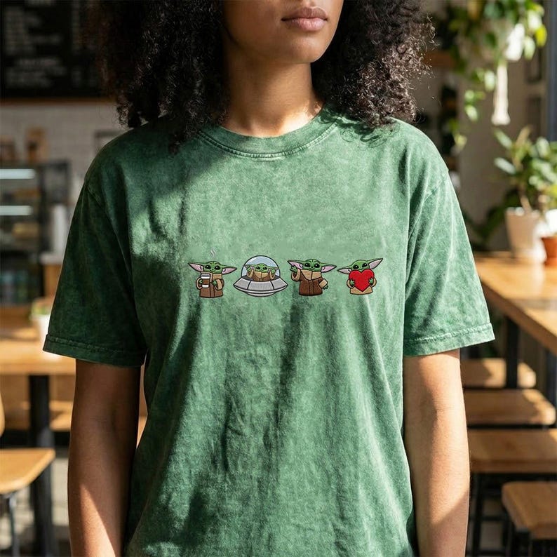 May include: Green t-shirt featuring four cartoon images of a character. The character is depicted in various poses, including holding a cup, inside a spaceship, wearing a brown coat, and holding a heart. The t-shirt has a vintage, washed appearance.