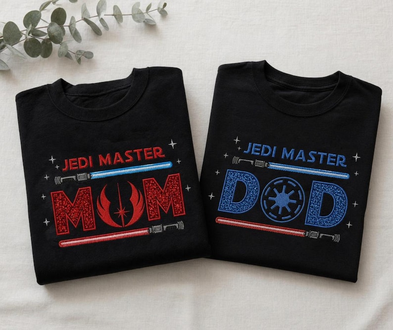 May include: Two black t-shirts with the words "JEDI MASTER" above the words "MOM" and "DAD" in red and blue, respectively. The "MOM" shirt features a red symbol, while the "DAD" shirt has a blue symbol. Both shirts have lightsaber designs.