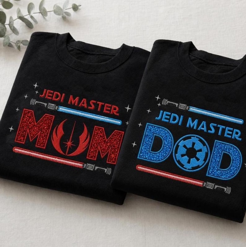 May include: Two black t-shirts with "JEDI MASTER" and lightsaber designs. One shirt says "MOM" in red glitter, the other says "DAD" in blue glitter with a circular emblem. A fun gift for Star Wars fans.