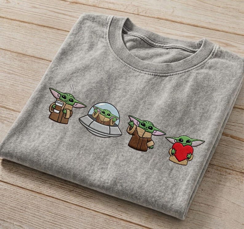 May include: A gray t-shirt featuring embroidered images of Grogu from The Mandalorian. The designs include Grogu holding a cup, in a spaceship, wearing a cloak, and holding a heart. The shirt is made of a soft material.
