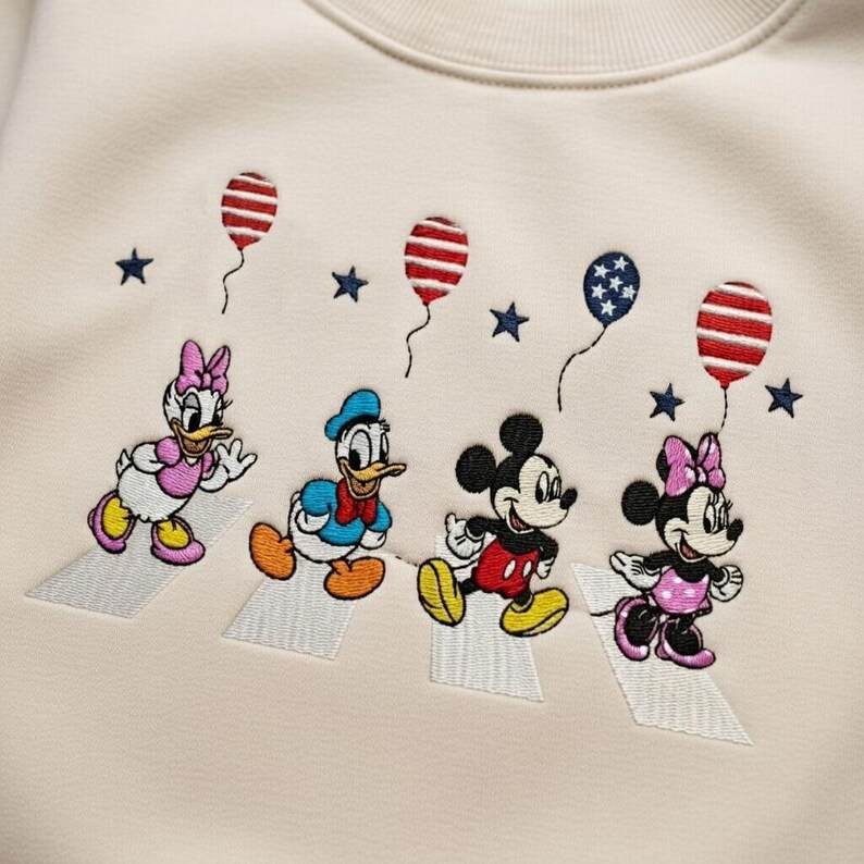 Puede incluir: Sudadera color crema con bordados de los personajes de Disney Daisy Duck, Donald Duck, Mickey Mouse y Minnie Mouse cruzando un paso de cebra. Globos y estrellas rojos, blancos y azules bordados.