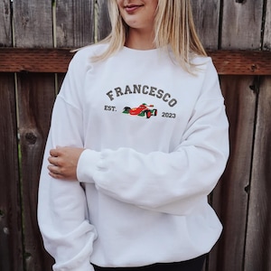 Puede incluir: Sudadera blanca con el nombre "Francesco" en letras grises arqueadas sobre el pecho. Debajo del nombre est&aacute; "EST. 2023" y un gr&aacute;fico de coche de carreras rojo y verde.