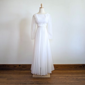 Puede incluir: Un vestido blanco de manga larga con un corpiño ajustado y una falda fluida. El vestido tiene un diseño simple y elegante y es perfecto para una boda u otra ocasión especial.