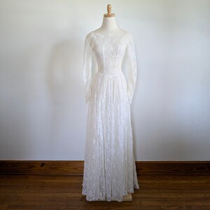 Puede incluir: Un vestido de novia de encaje blanco con mangas largas y un corpi&ntilde;o ajustado. El vestido tiene una falda completa y se muestra en un maniqu&iacute;.