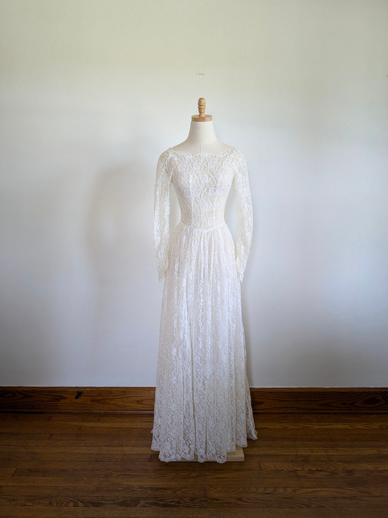Puede incluir: Un vestido de novia de encaje blanco con mangas largas y un corpi&ntilde;o ajustado. El vestido tiene una falda completa y se muestra en un maniqu&iacute;.