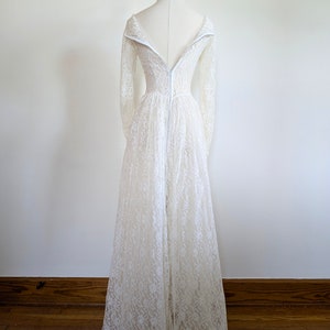 Puede incluir: Un vestido de novia de encaje blanco con mangas largas y cremallera en la espalda. El vestido tiene un corpi&ntilde;o ajustado y una falda fluida.