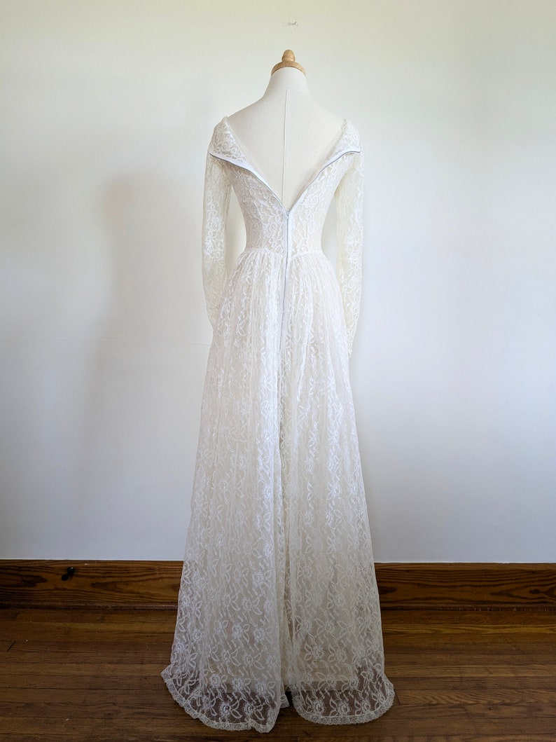 Puede incluir: Un vestido de novia de encaje blanco con mangas largas y cremallera en la espalda. El vestido tiene un corpi&ntilde;o ajustado y una falda fluida.