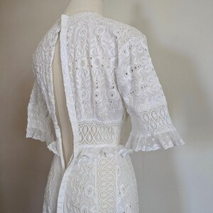 May include: White eyelet lace dress with a fitted bodice and a flowing skirt. The dress has a keyhole back and short sleeves with ruffles.