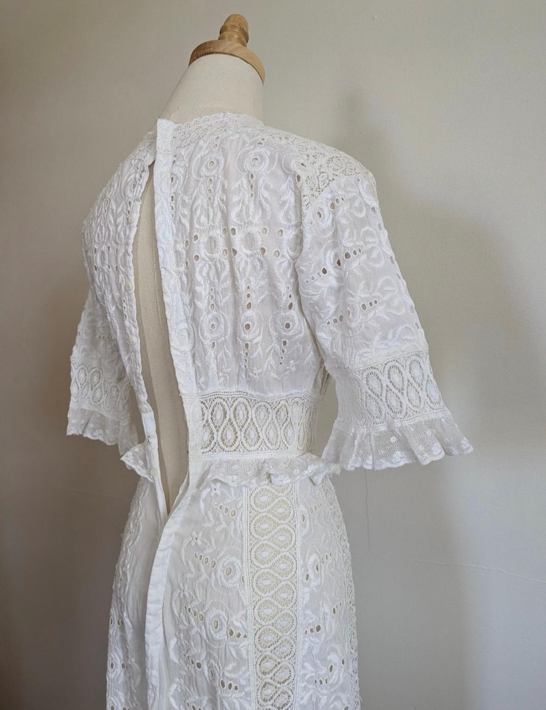 May include: White eyelet lace dress with a fitted bodice and a flowing skirt. The dress has a keyhole back and short sleeves with ruffles.