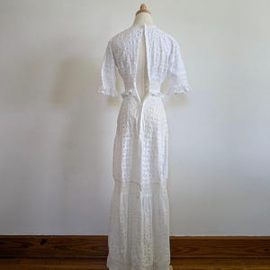 May include: White eyelet maxi dress with a low back and a fitted bodice. The dress has a tiered skirt and short sleeves.