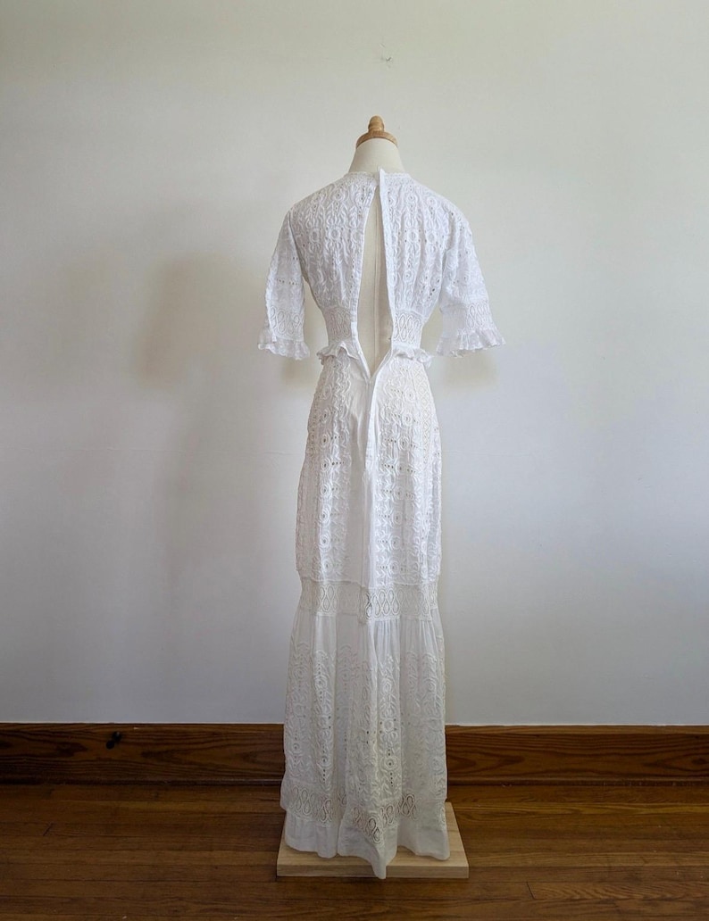 May include: White eyelet maxi dress with a low back and a fitted bodice. The dress has a tiered skirt and short sleeves.
