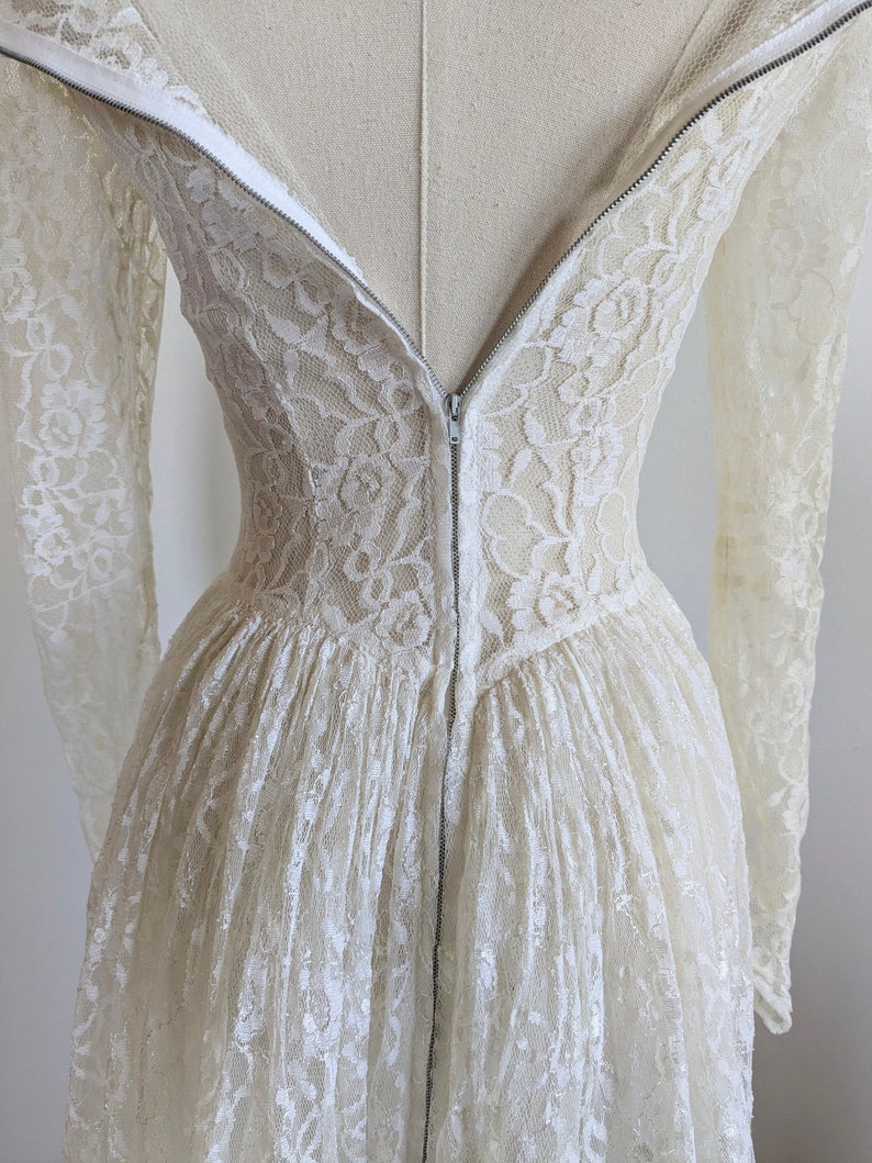Puede incluir: Un vestido blanco de encaje con mangas largas y una cremallera en la espalda.