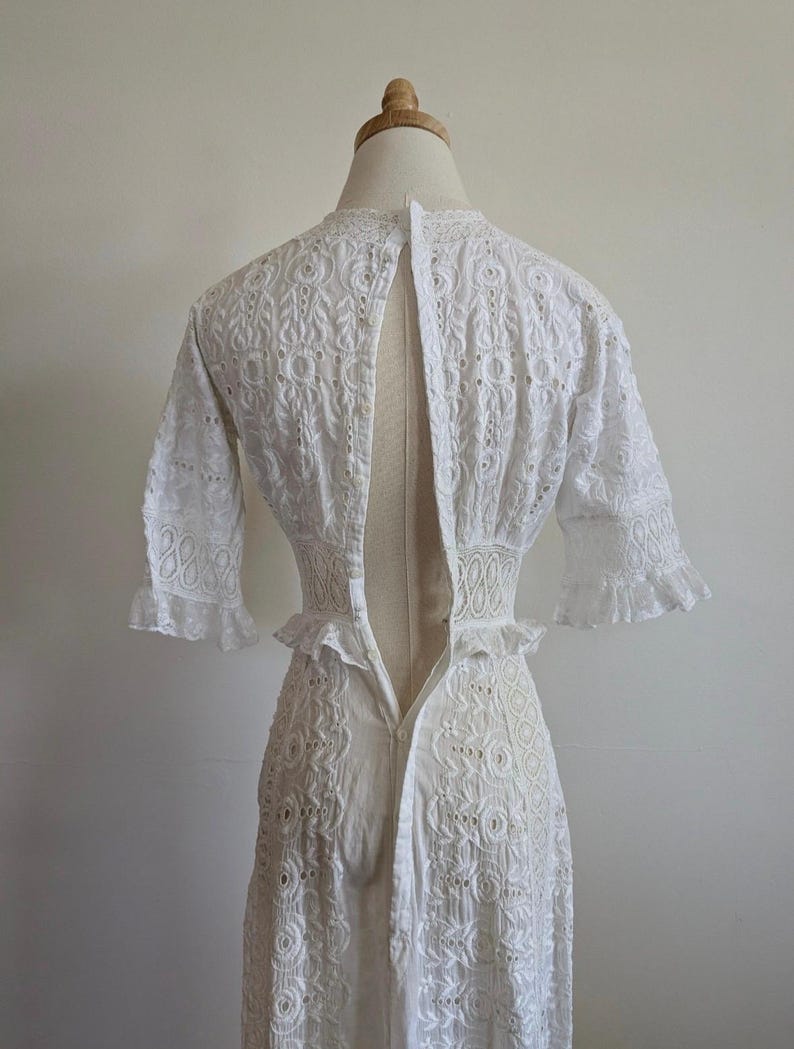 May include: White eyelet dress with a low back and a zipper closure. The dress has a fitted bodice and a flowing skirt.