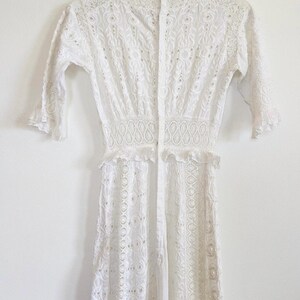 May include: White eyelet dress with a button-up front and a ruffled hem. The dress has a fitted bodice and a flowy skirt.