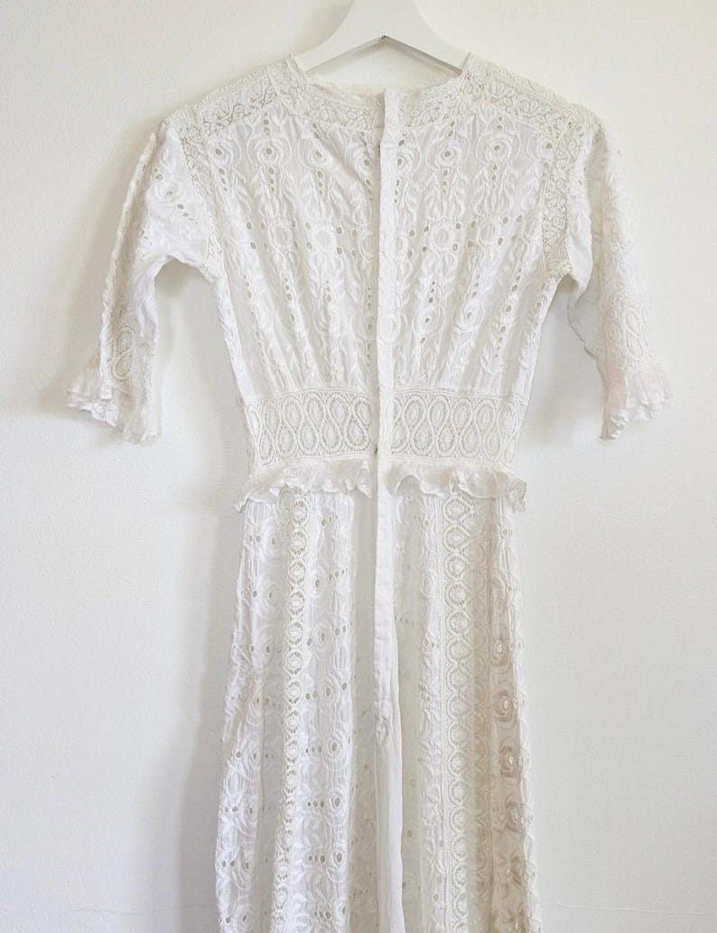 May include: White eyelet dress with a button-up front and a ruffled hem. The dress has a fitted bodice and a flowy skirt.