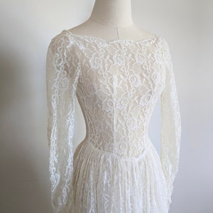 Puede incluir: Un vestido de novia de encaje blanco con mangas largas y un corpi&ntilde;o ajustado. El vestido tiene un escote redondo y una falda completa.