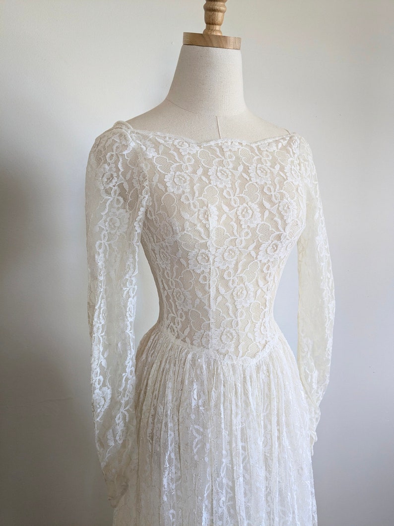 Puede incluir: Un vestido de novia de encaje blanco con mangas largas y un corpi&ntilde;o ajustado. El vestido tiene un escote redondo y una falda completa.