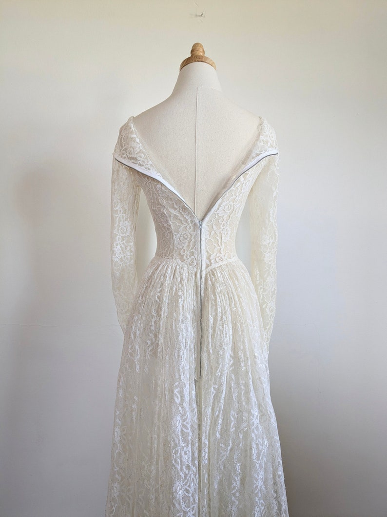 Puede incluir: Un vestido de novia de encaje blanco con mangas largas y una cremallera en la espalda.